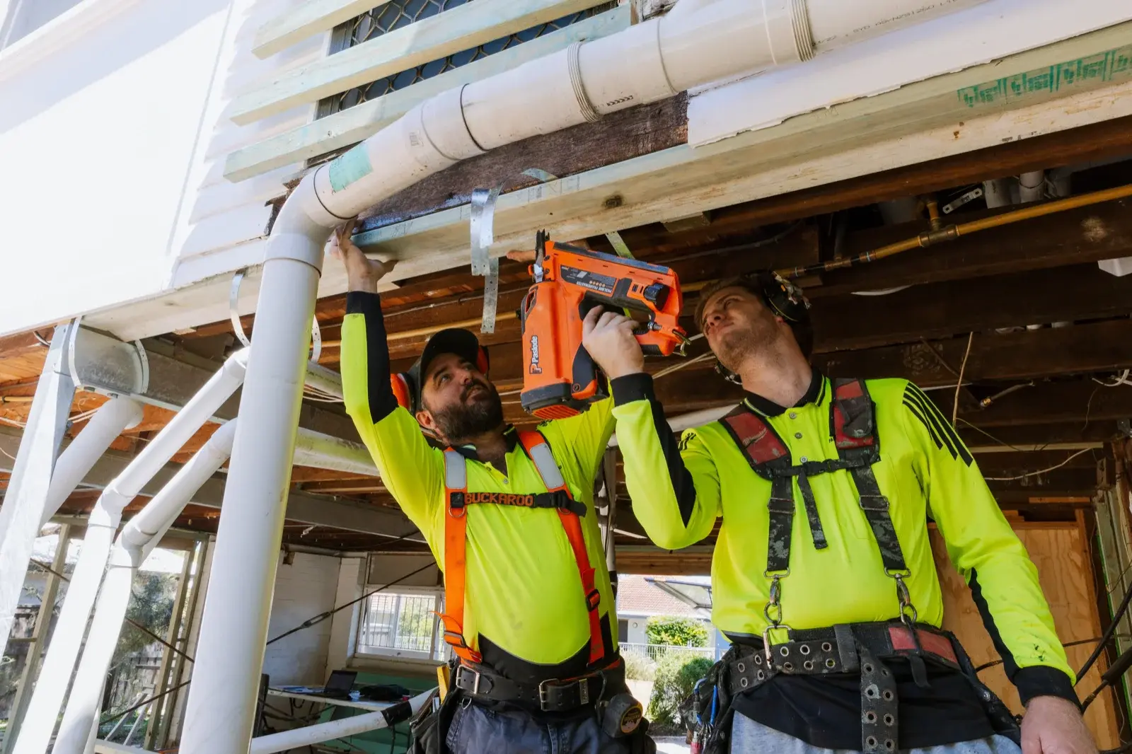 Two Farr Constructions tradesmen working together to install pipework on a Brisbane renovation — demonstrating coordinated on-site team management