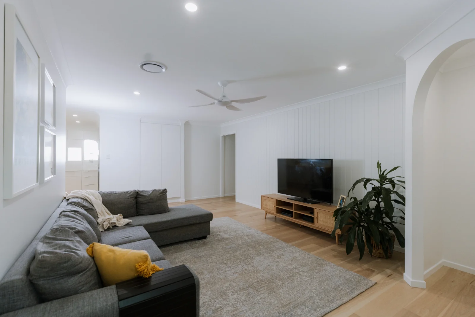 Completed living room renovation Brisbane — bright open-plan interior with timber floors, arch detail and TV unit by Farr Constructions